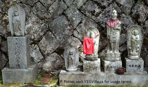 The bibs on these statues are Jizō (地蔵), Buddhist guardian figures; dressing them is a deeply rooted act of care, protection, and remembrance for lost children or an act of servitude to the community, 2026-04-05, Imabari Castle, P. Potter.