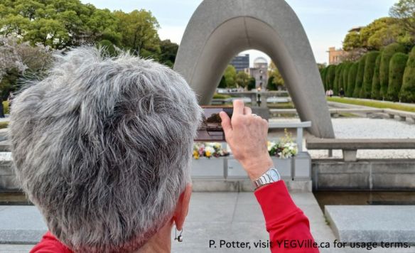 A visitor capturing an image of the Atomic Bomb Dome through the Hiroshima Victims Memorial Cenotaph 広島平和都市記念碑（原爆死没者慰霊碑), Hiroshima environ, 2026-04-11, P. Potter.