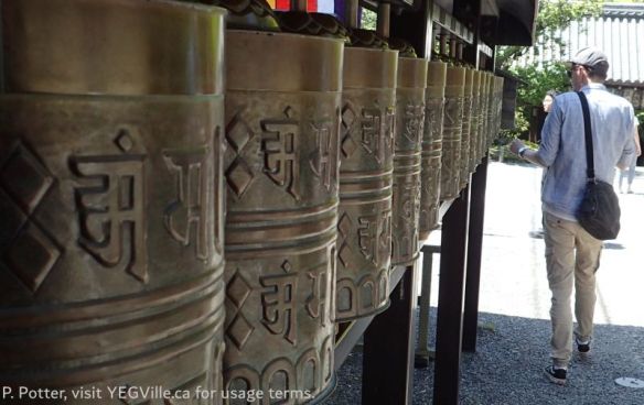 A visitor spinning the prayer wheels or 回転式経蔵 (kaiten‑shiki kyōzō), they are a cylindrical drum mounted on a vertical axis that you spin by hand which is believed to have the same merit as reciting the sutra itself; 2026-04-16, Toji Temple environ, Kyoto Japan, P. Potter.